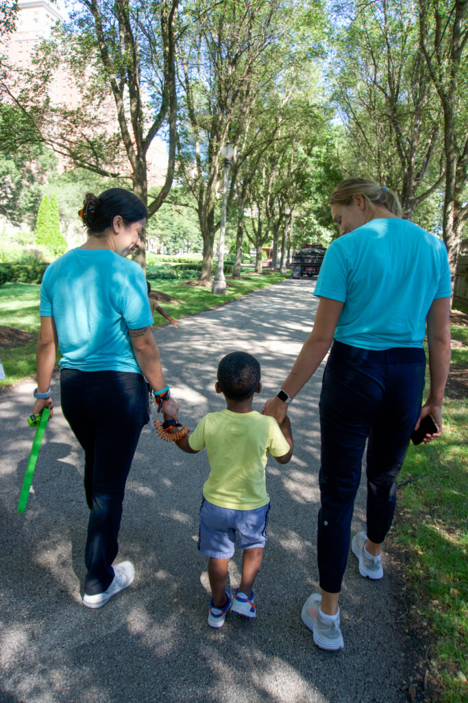 Stride team members walking hand in hand with a young child in blue shirt and blue shorts at the park. 